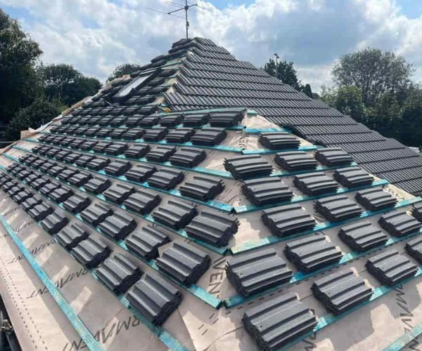 This is a photo of a new hip roof being installed. New felt, battens, and grey tiles have been installed, also a new velux window. Works carried out by FDC Roofing Finedon