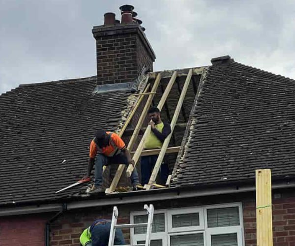 This is a photo of a roof repair being carried out. A section of the roof has been stripped and two roofers are replacing the rafters. Works being carried out by FDC Roofing Finedon